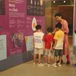 A group of school children with teacher in front of a panel in an exhibition
