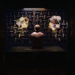 Visitor viewing an immersive installation featuring illuminated floral displays and geometric acoustic-style wall panels.