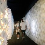 Young visitor walking through an illuminated corridor with honeycomb-patterned walls in the Be section of the exhibition.