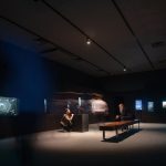 Visitors exploring the Bees: A Story of Survival exhibition, viewing displays and digital interpretation in a darkened gallery.