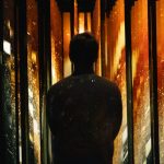 Visitor experiencing SWARM, an immersive installation featuring illuminated vertical panels and dynamic amber and gold light patterns.