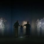 A child and two adults interact with immersive projections of swirling light and particles in the Symphony exhibition experience.